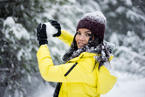 Girl making snowball in the forest wearing a bright yellow jacket