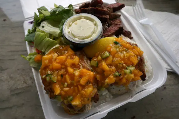 Fresh Ono with Papaya-mango salsa, Steak, white rice, and tossed greens Island style Plate lunch on a white table.