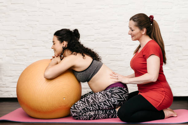 parteira massageando uma mulher grávida durante o exercício com uma bola de fitness - human pregnancy massaging midwife prenatal care - fotografias e filmes do acervo