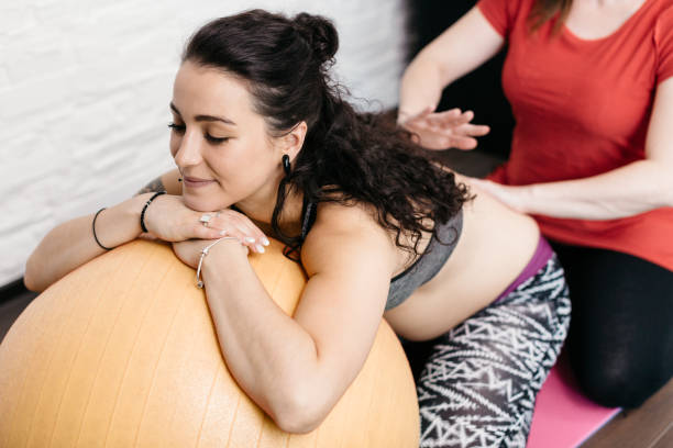 uma mulher grávida, recebendo uma massagem nas costas de sua parteira - human pregnancy massaging midwife prenatal care - fotografias e filmes do acervo