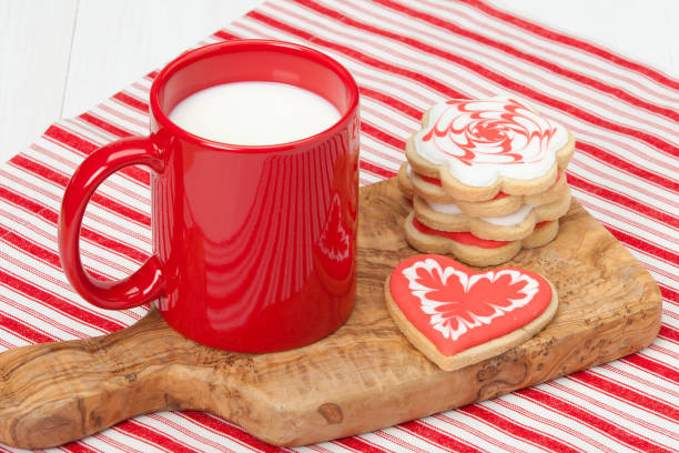 Sugar biscuits with Be Mine phrase on plate near cup of coffee full of marshmallow with grated cinnamon on pastel pink background. Variant of coffee serving for Valentines Day celebration.