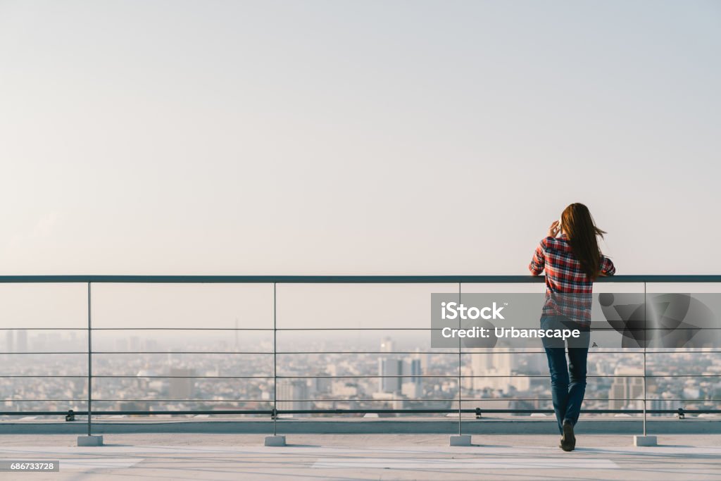 Woman using mobile phone at rooftop during sunset with copy space, communication or lonely people concept Rooftop Stock Photo