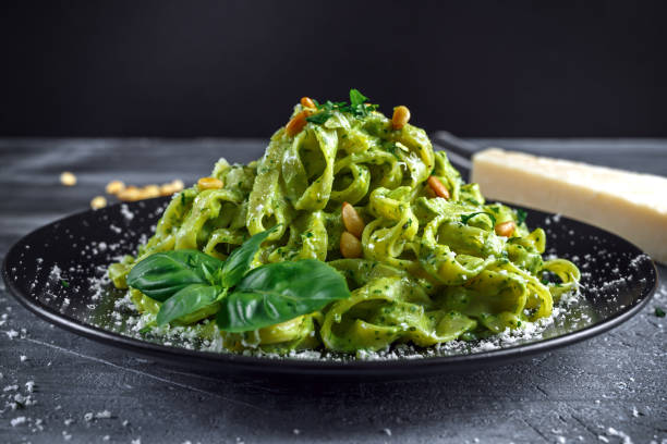 Tagliatelle pasta with pesto sauce, pine nuts and parmesan on black plate.