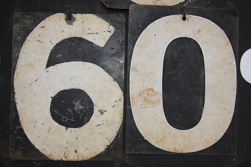 White numbers depicting the number 60 on a battered old cricket scoreboard.