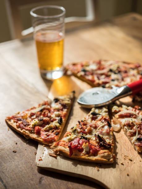 Home made oven baked Pizza with variety of topings on the wooden table with pizza cutter. Glass of Lager beer in the background.