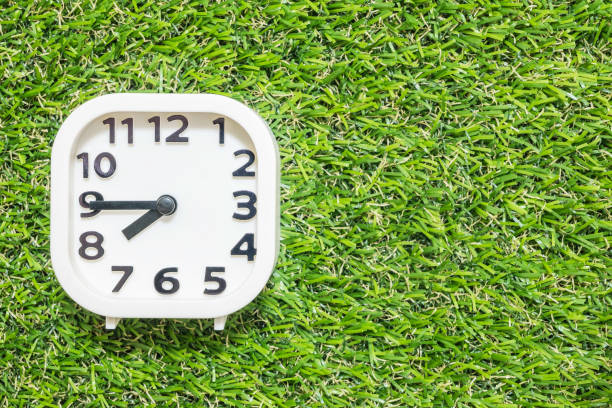 istock Closeup white clock for decorate show a quarter to eight or 7:45 a.m. on green artificial grass floor textured background with copy space 686834700