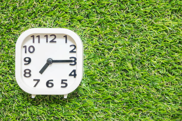istock Closeup white clock for decorate show a quarter past seven or 7:15 a.m. on green artificial grass floor textured background with copy space 686835128