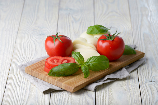 Mozzarella and tomato with basil leaves on a white wooden background