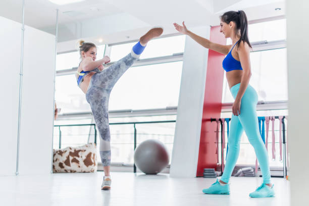 istock Young Caucasian woman training with a personal trainer in gym practicing high side kicks. 686886284