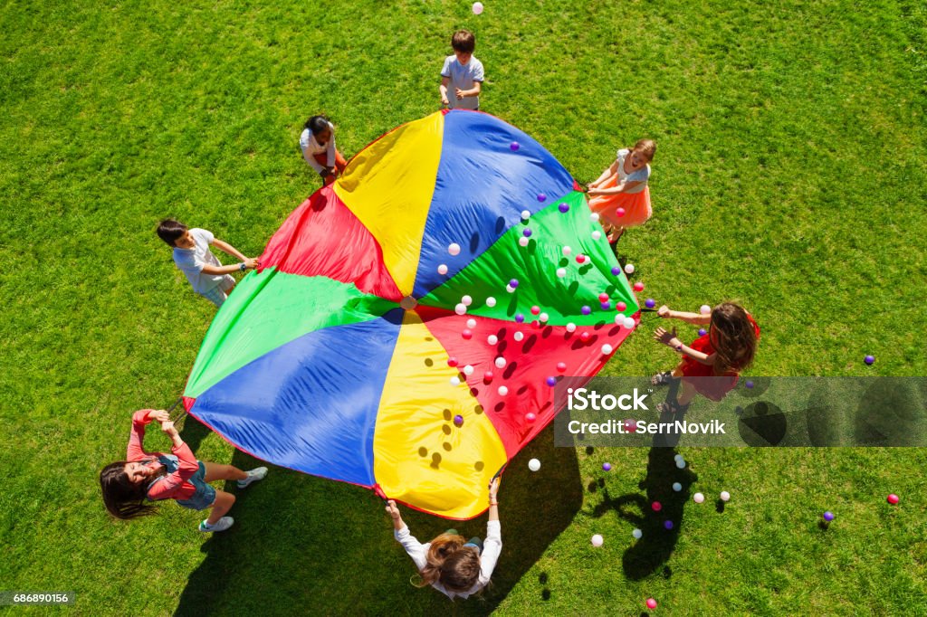 Niños felices agitando paracaídas arco iris lleno de bolas - Foto de stock de Niño libre de derechos