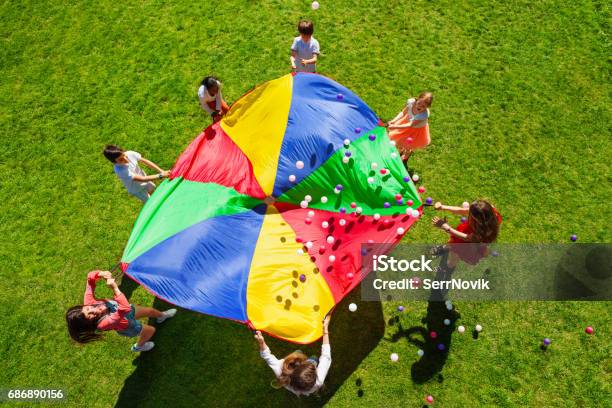 Niños Felices Agitando Paracaídas Arco Iris Lleno De Bolas Foto de stock y más banco de imágenes de Niño