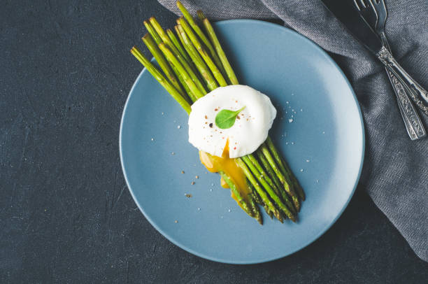 istock Green asparagus and boiled poached egg on a blue plate over a dark concrete background 686896444