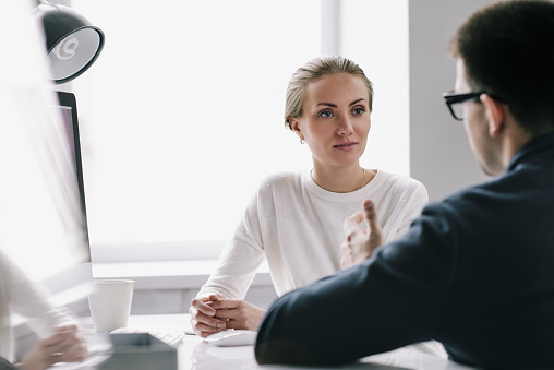 Waist-up portrait of confident young HR manager sitting at office desk while conducting interview with applicant for position