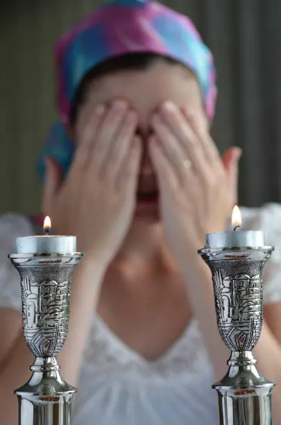 Jewish woman says the blessing upon lighting the sabbath candles before shabbat eve dinner.