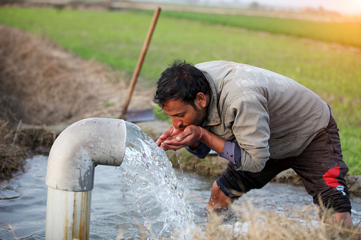 Young men of Indian ethnicity drinking water outdoor in the field.