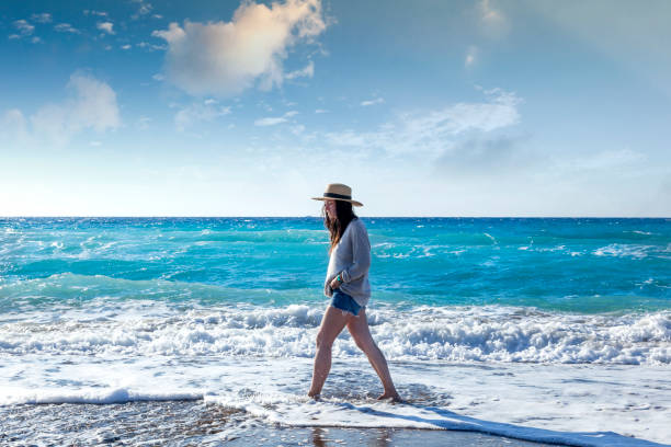 Young woman in a hat walking along the seashore. Holidays and travel.