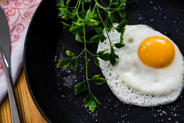 istock Fried egg in a black cast-iron pan without oil, sprinkled with salt with fresh parsley. 686967920