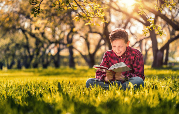 istock Cute boy reading a book sitting in the park at sunset 686976002