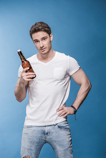 Handsome young man holding beer bottle and looking at camera