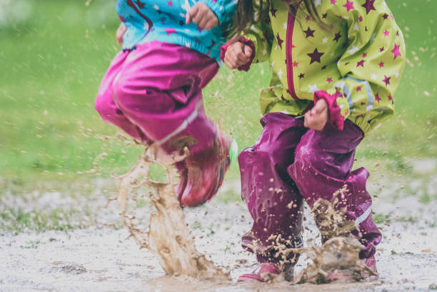 istock Children in rubber boots and rain clothes jumping in puddle. 687037714