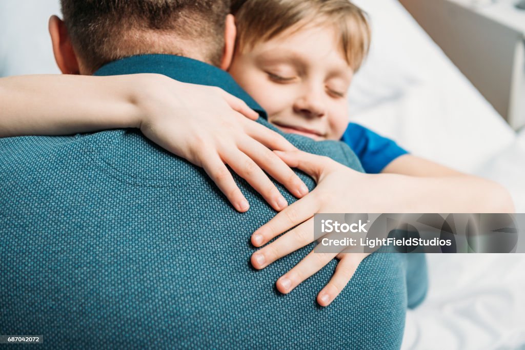 Porträt von lächelnden kleinen Sohn umarmt Vater im Krankenhaus Kammer - Lizenzfrei Umarmen Stock-Foto