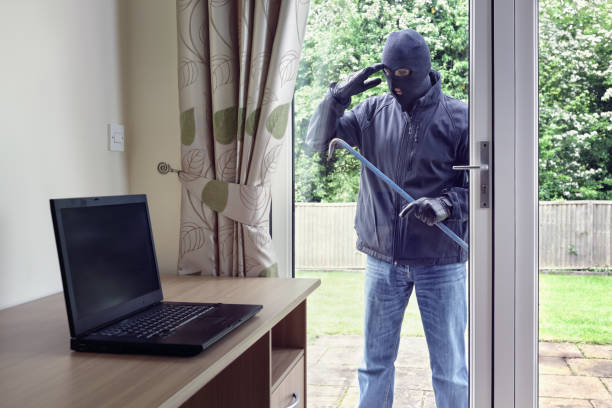 Thief looking through patio doors window at a laptop computer to steal Thief breaking into a house via a patio doors window with a crowbar to steal a laptop computer from an office desk burglar stock pictures, royalty-free photos & images