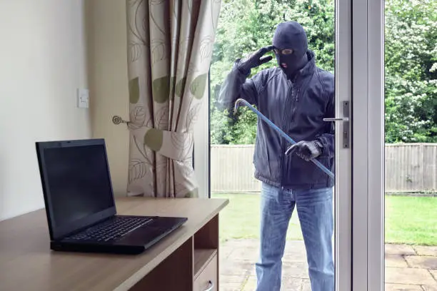 Photo of Thief looking through patio doors window at a laptop computer to steal