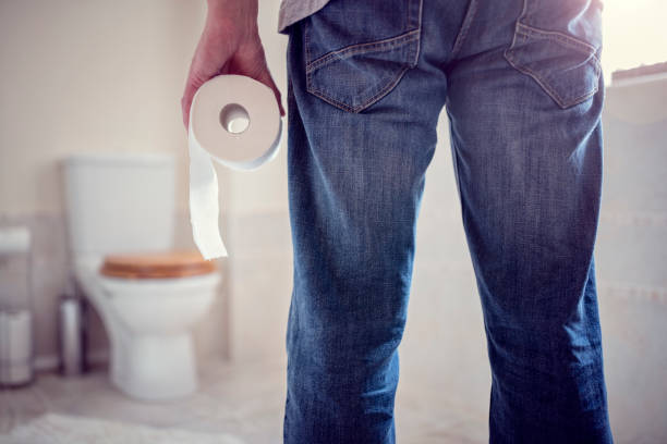 Man holding toilet paper roll in bathroom Man holding toilet tissue roll in bathroom looking at loo Male Toilet stock pictures, royalty-free photos & images