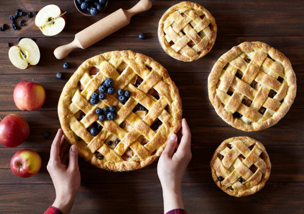 istock Apple pie on the kitchen wooden table with apples and rolling pin. Hands in the frame. Traditional dessert for Independence Day. Dark food photo 687060364