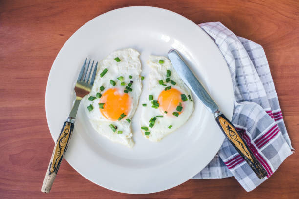 istock Fried eggs in white plate on napkin at wooden background, top view 687068218