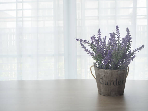 istock wood table with left free space and purple lavender flowerpot on beautiful white drape window texture background. 687068286