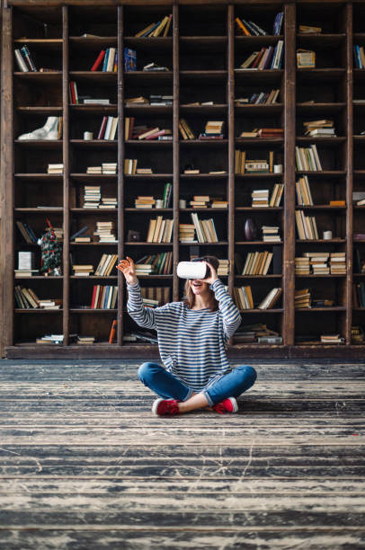 Happy woman wearing VR Glasses in front of bookshelves stock photo