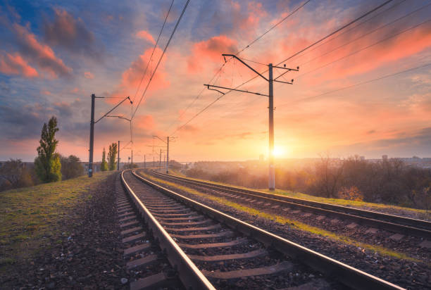 chemin de fer et beau ciel au coucher du soleil. paysage industriel avec la gare, ciel bleu coloré avec des nuages rouges, arbres et herbe verte, lumière du soleil jaune en été. jonction ferroviaire. industrie - transport ferroviaire photos et images de collection