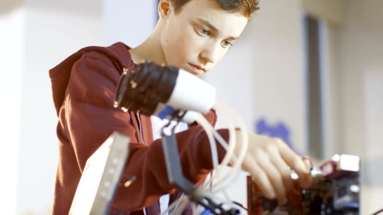 Boy Works on a Fully Functional Programable Robot with Bright LED Lights for His School Robotics Club Project.