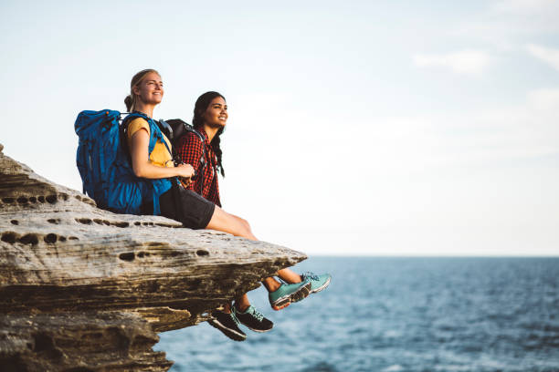 backpackers sitting at the edge of beautiful cliff - hiking coastline waters edge sunny imagens e fotografias de stock