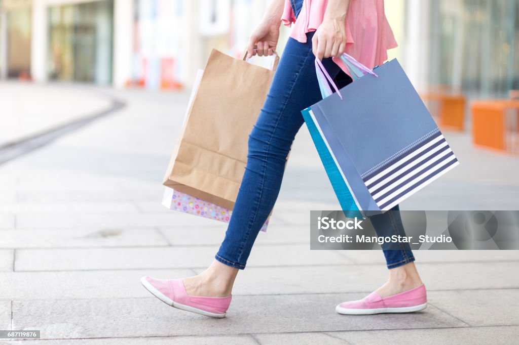 Young Caucasian woman walking with shopping bags Young Caucasian woman wearing jeans holding shopping bags and walking in street Shopping Bag Stock Photo