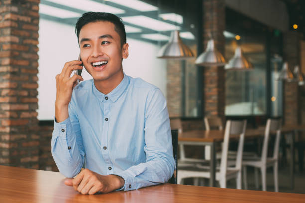 istock Smiling Asian Man Talking on Phone at Cafe Table 687159644