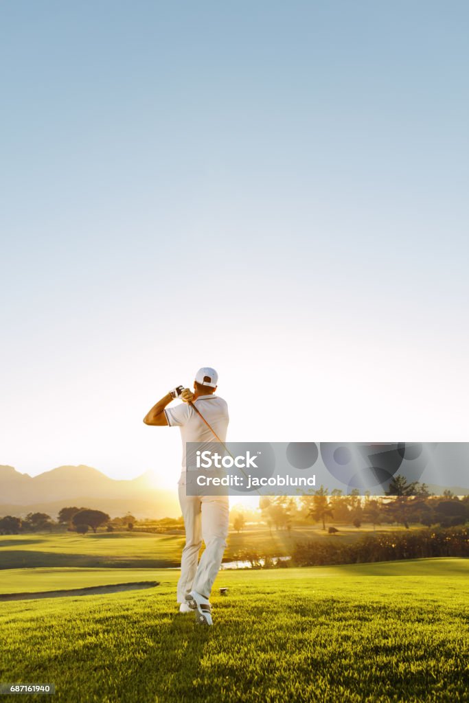 Young man playing golf on a sunny day Rear view of golfer hitting driver on a golf course in the sun. Full length shot of young man playing golf on a sunny day. Golf Stock Photo