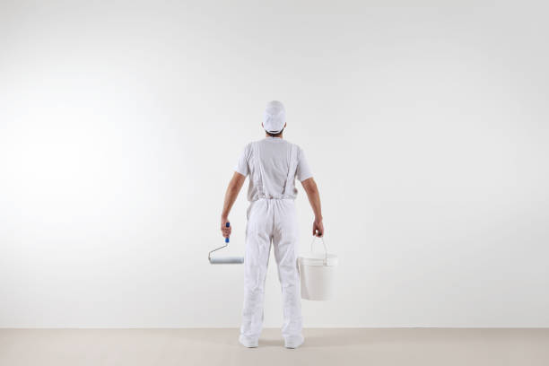 Rear view of painter man looking at blank wall, with paint roller and bucket, isolated on white room