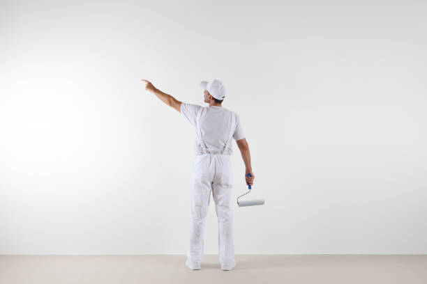 istock Rear view of painter man pointing with finger the blank wall, with paint roller, isolated on white room 687166572