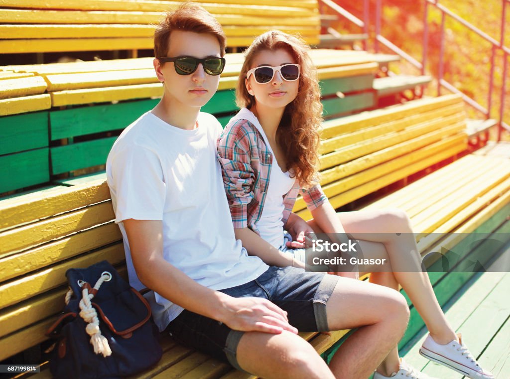 Fashion young couple teenagers are resting in the city on the bench at summer sunny day Adult Stock Photo