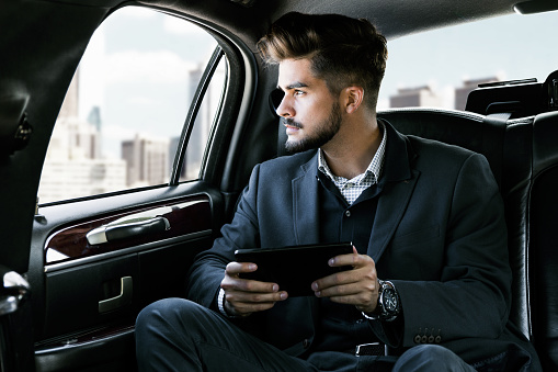 Casual businessman on mobile phone in rear of the car researching market on tablet information device