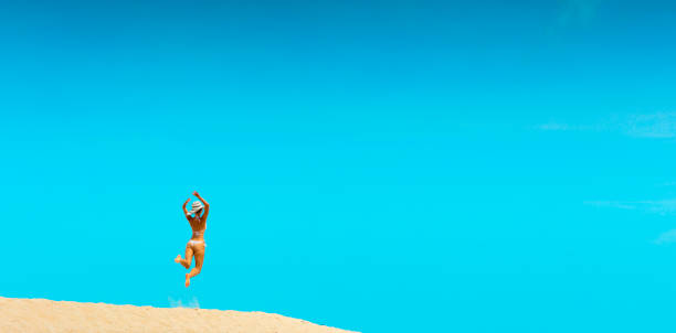 A women jumping off a sand dune with the sun shining in the sky.