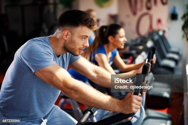 Young Man And Woman Warming Up On Bikes In The Gym Stock Photo - Download Image Now - Cycling, Cardiovascular Exercise, Exercise Bike