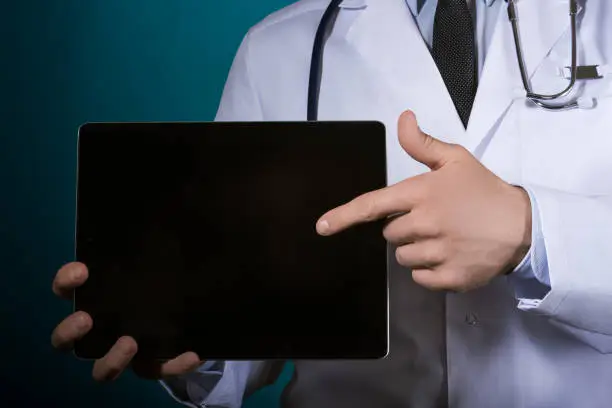 Photo of Doctor with a stethoscope in a white coat indicates a finger on the tablet.