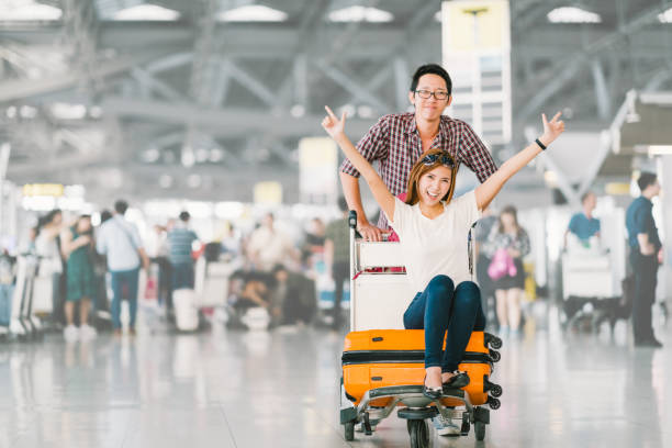 若いアジアの観光客カップル幸せと一緒に座っていると荷物のトロリーまたは荷物のカートに応援のガール フレンド、旅行の興奮。休日休暇旅行コピー スペースを持つ、海外のコンセプト - luggage cart ストックフォトと画像