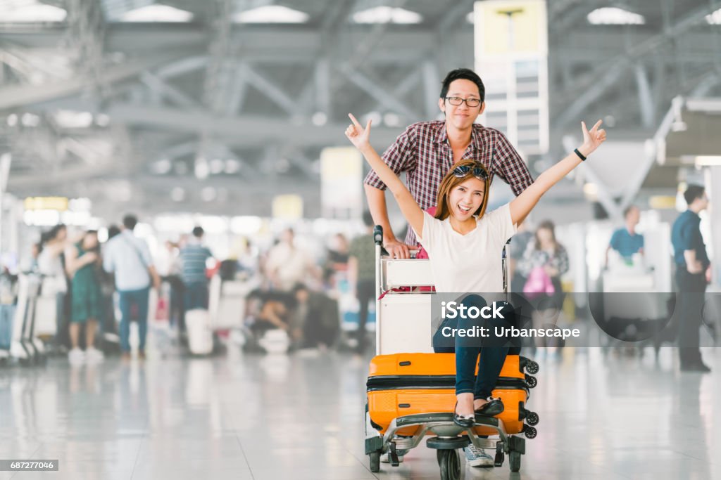 Young Asian tourist couple happy and excited together for the trip, girlfriend sitting and cheering on baggage trolley or luggage cart. Holiday vacation travelling abroad concept, with copy space Airport Stock Photo