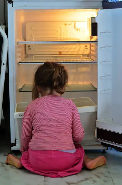 Hungry Poor little girl looks for food in an empty fridge at home.