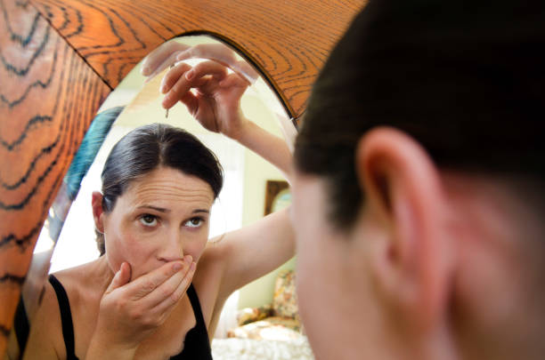 Woman Going Gray Young caucasian woman looks in the mirror and plucks a grey hair from her head. . gray hair young woman stock pictures, royalty-free photos & images