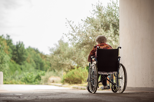 Vista posterior de mujer Senior en silla de ruedas en el pasillo del garaje photo